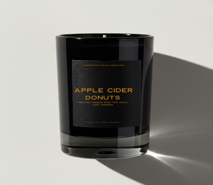 Black candle with 'Apple Cider Donuts' label on a light gray background