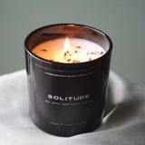 A Predominantly Black SOLITUDE CANDLE, with notes of sage, lavender, earthy woods, and lemon serenely burning to create a tranquil ambiance.