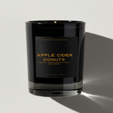 Black candle with 'Apple Cider Donuts' label on a light gray background