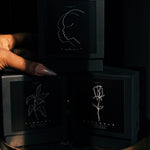 Core Trio Part I Candle Gift Set: black Core candle boxes stacked in a dark setting — Predominantly Black