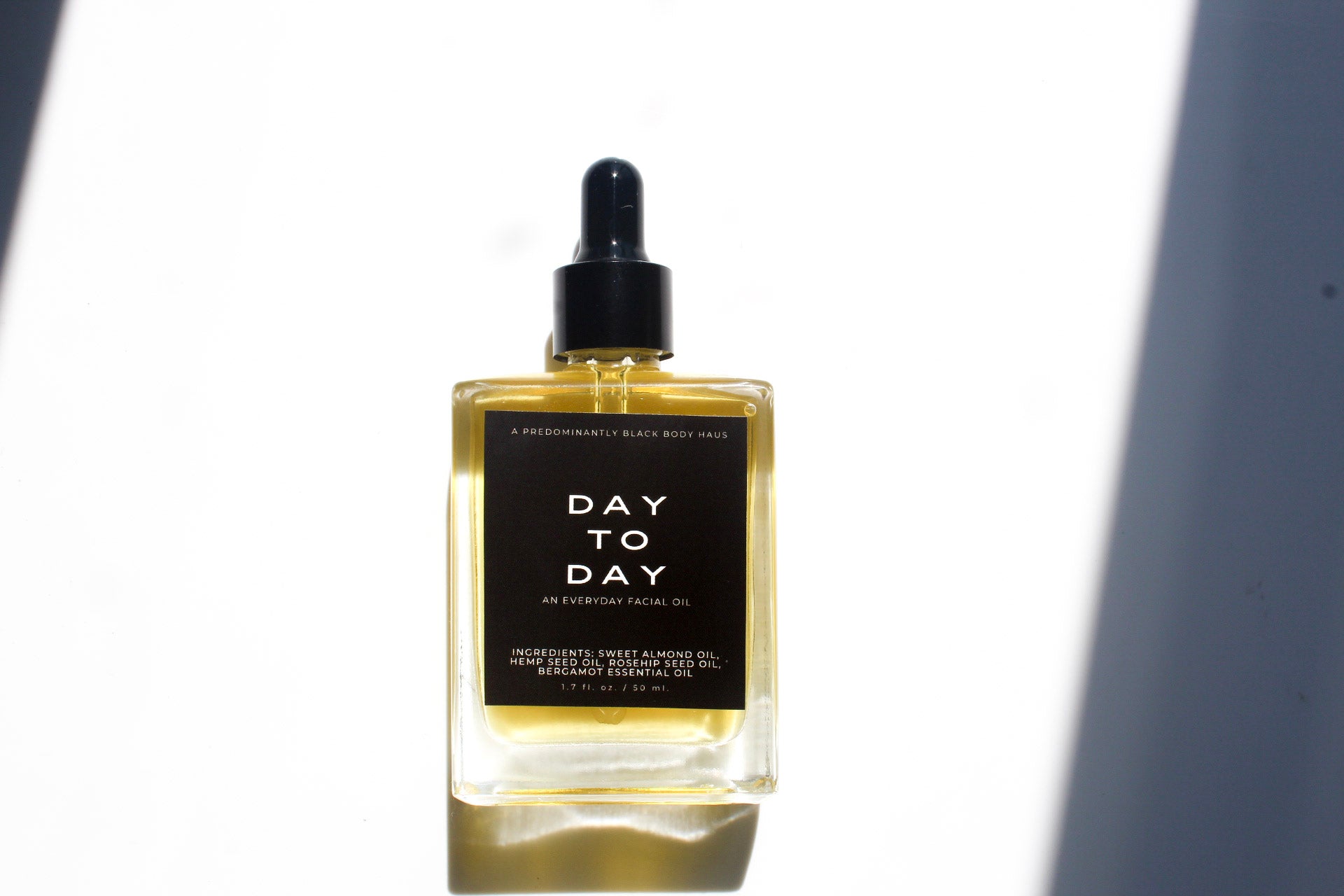 Skin Maintenance System: DAY-TO-DAY facial oil bottle in sunlight — Predominantly Black