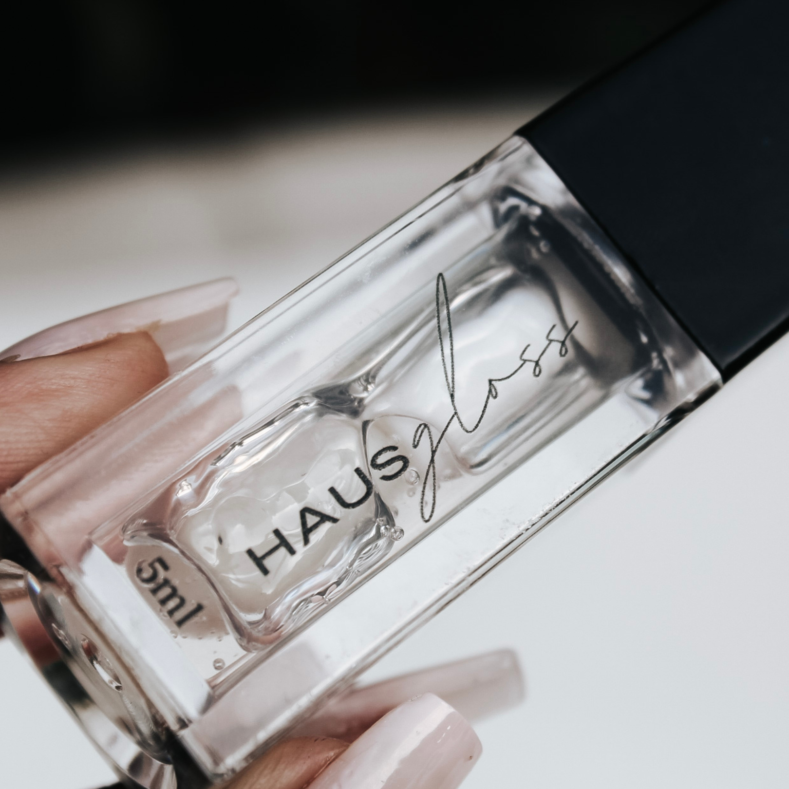 Hand holding a HAUS GLOSS bottle — Predominantly Black