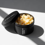 Open COCONUT HUSK & GINGER scented wax melt tin with yellow pieces; coconut husk and ginger fragrance — Predominantly Black