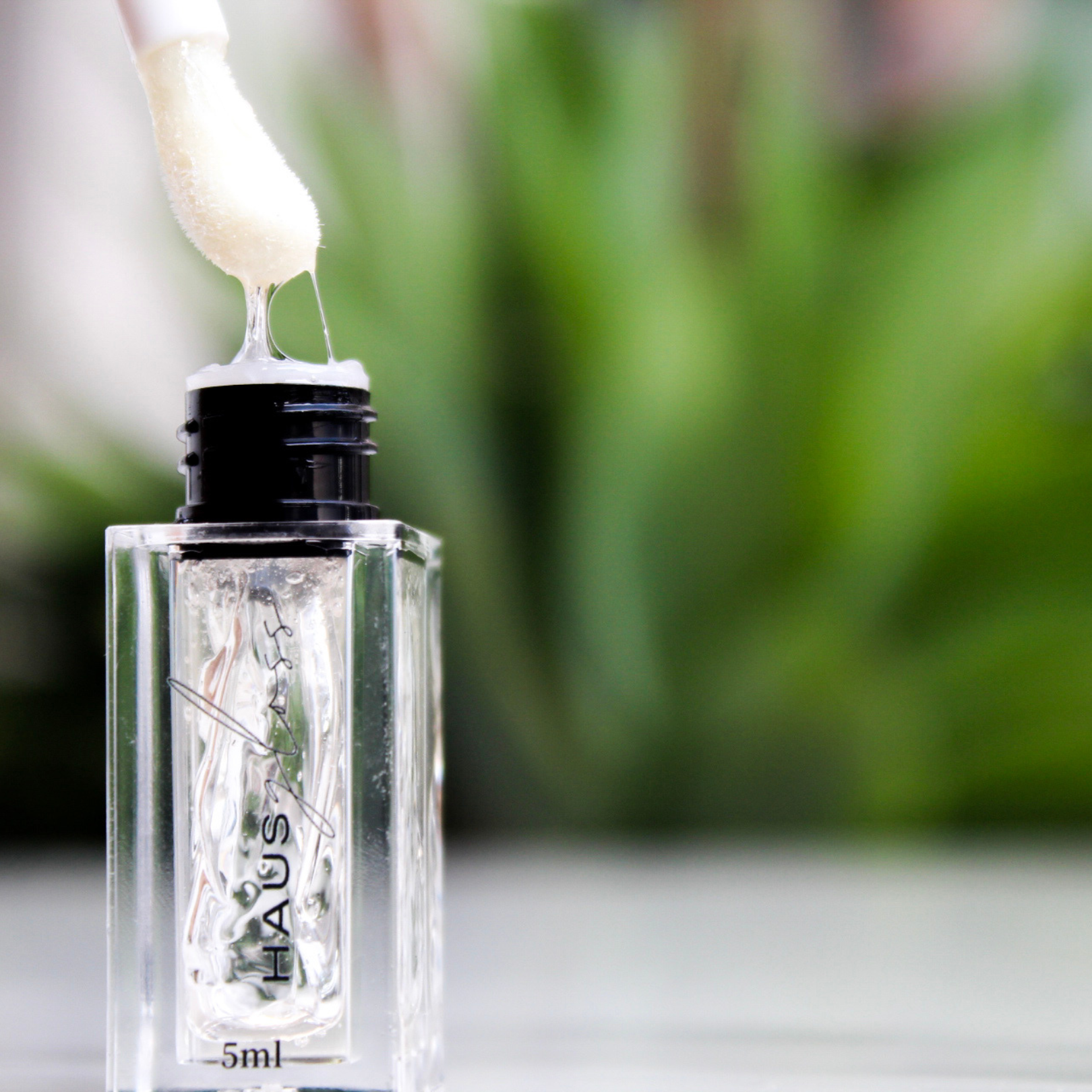 Open HAUS GLOSS bottle with applicator outdoors — Predominantly Black